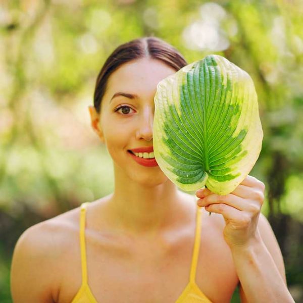 Girl in a summer park. Woman in a yellow top. Lady with green leaf near face.